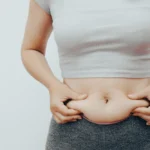 Mulher apertando a barriga com as mãos a fim de saber como desinchar o corpo
