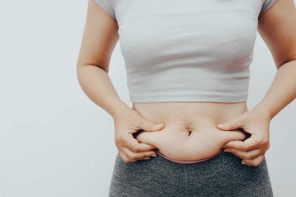 Mulher apertando a barriga com as mãos a fim de saber como desinchar o corpo